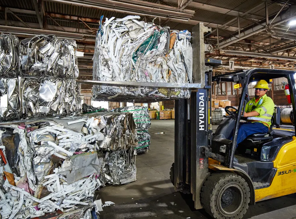 Forklift handling baled scrap metal inside recycling plant